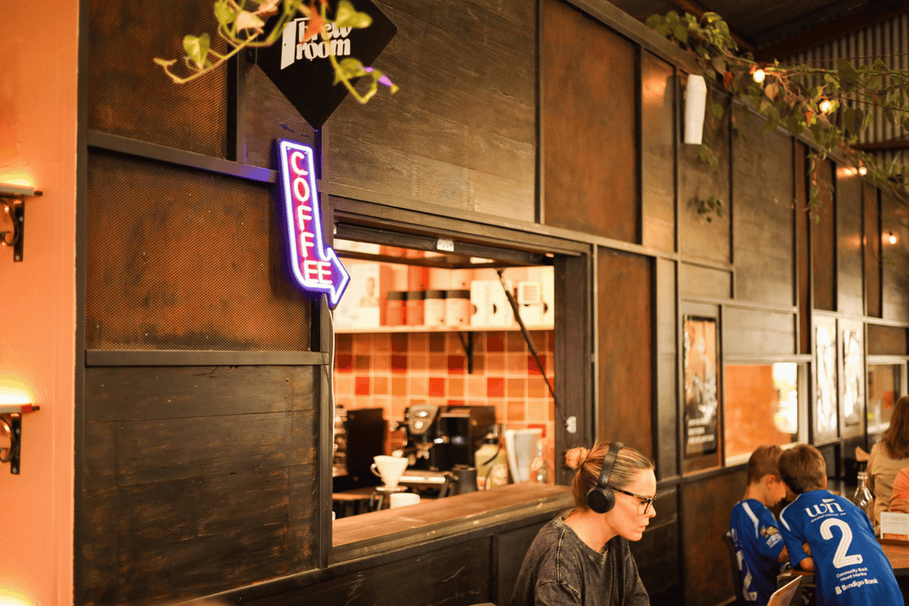 A cozy cafe interior with dark wood paneling, a neon 'COFFEE' sign, and patrons seated at a table in the foreground.